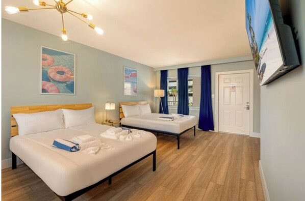 A hotel room with two beds, a wooden floor, a ceiling light fixture, and a door.