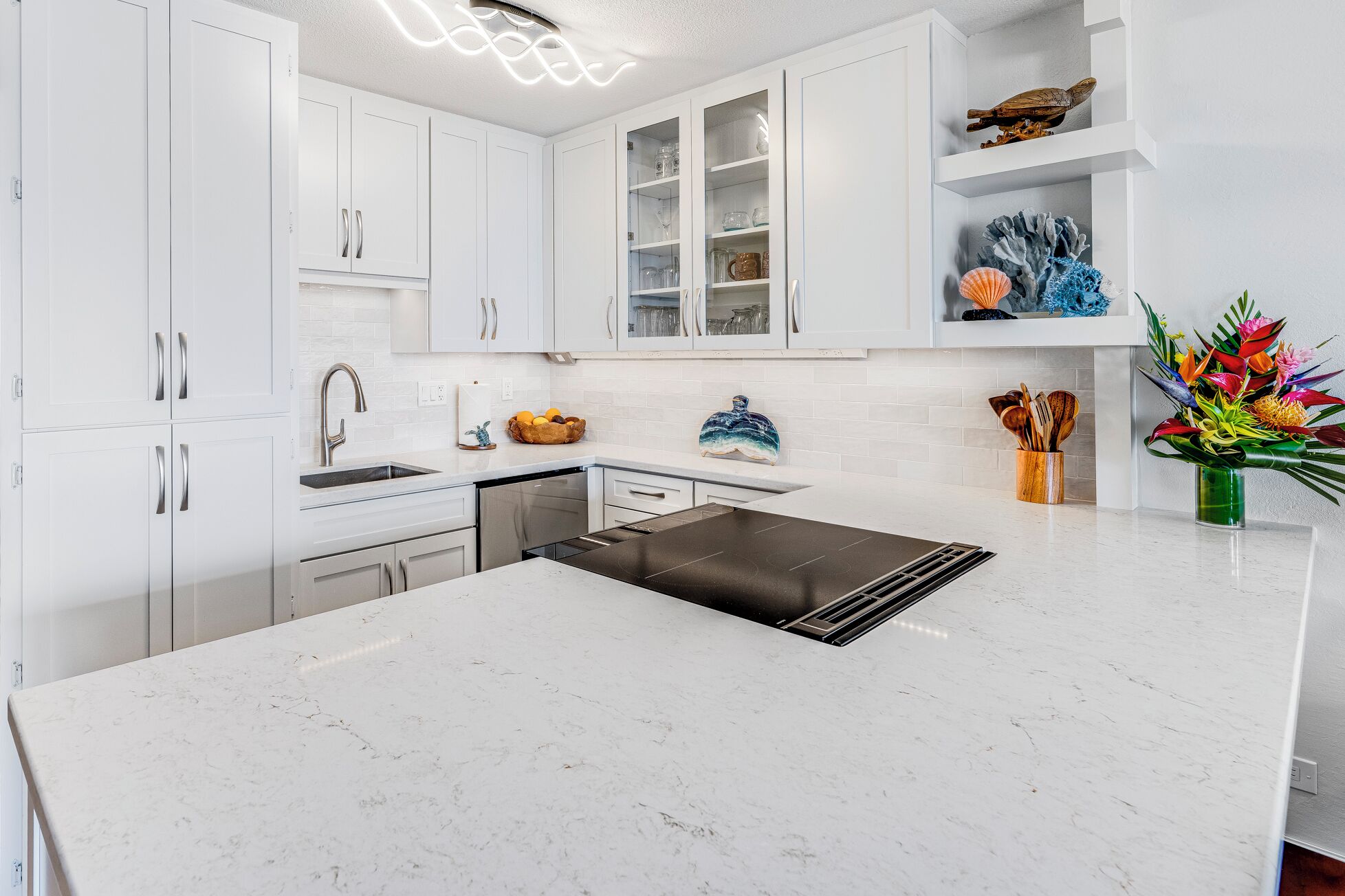 Een moderne keuken met witte kasten, een zwarte inductiekookplaat en een wit marmeren aanrecht.