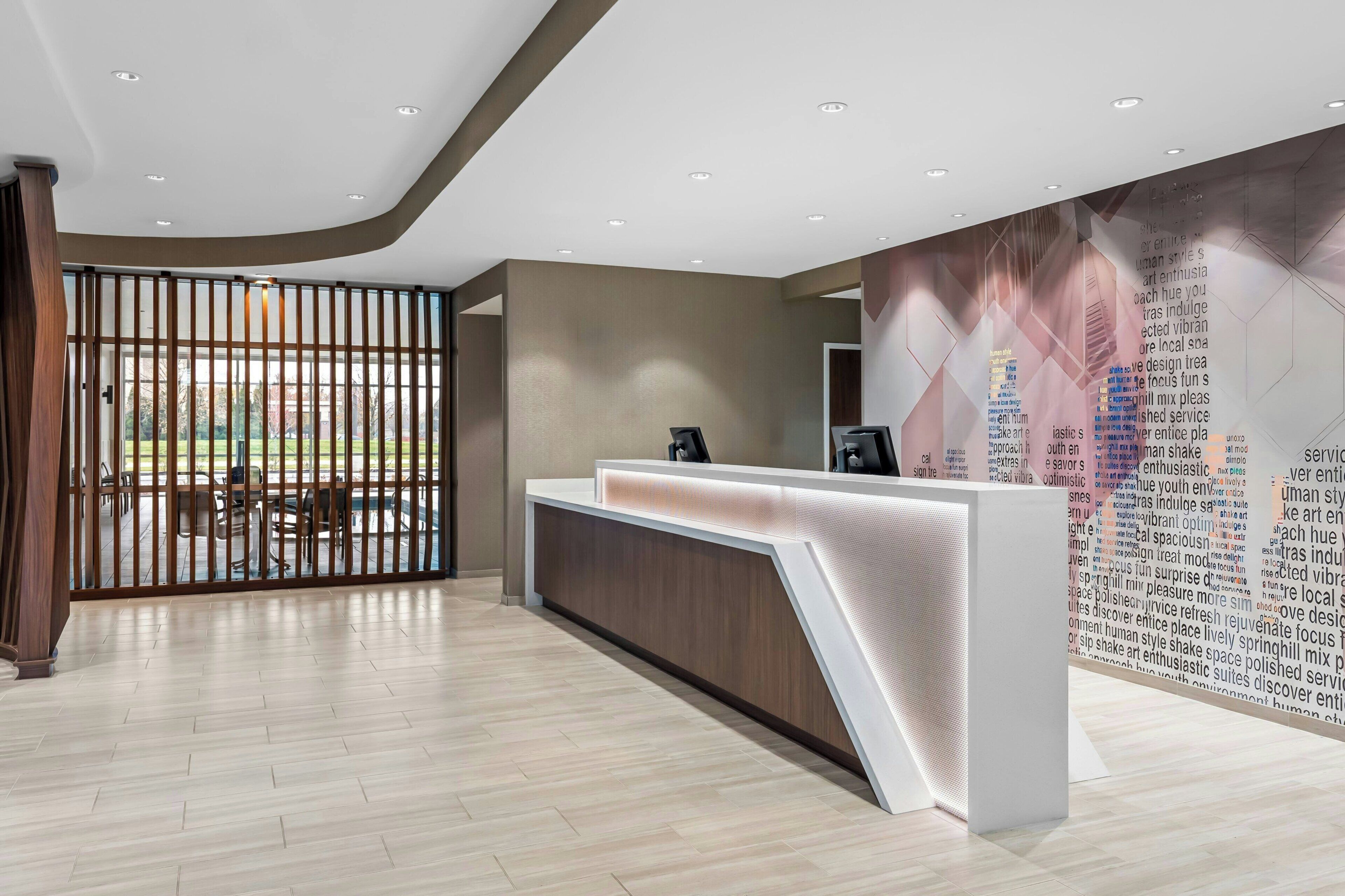 A modern reception area with a wooden reception desk, a glass partition, and a wall with a word cloud design.