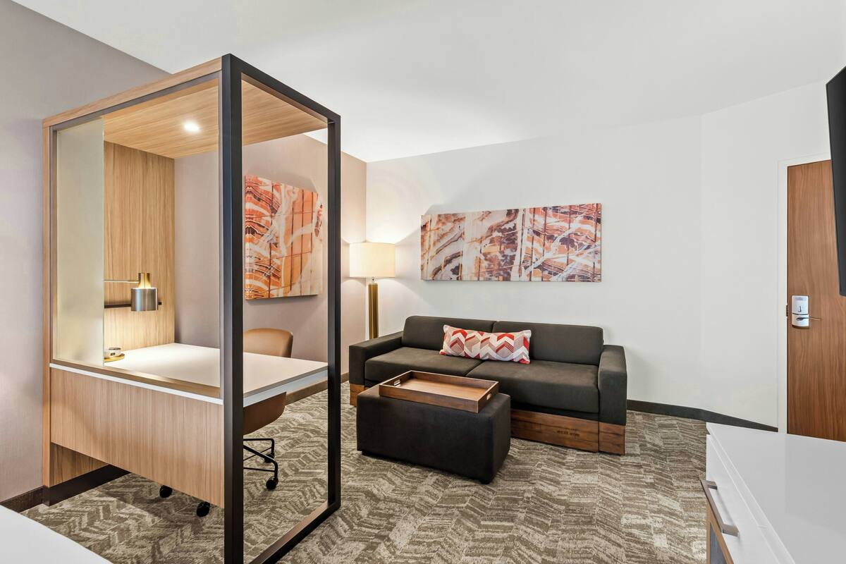 A modern hotel room with a desk, a sofa, a mirror, and artwork on the walls.