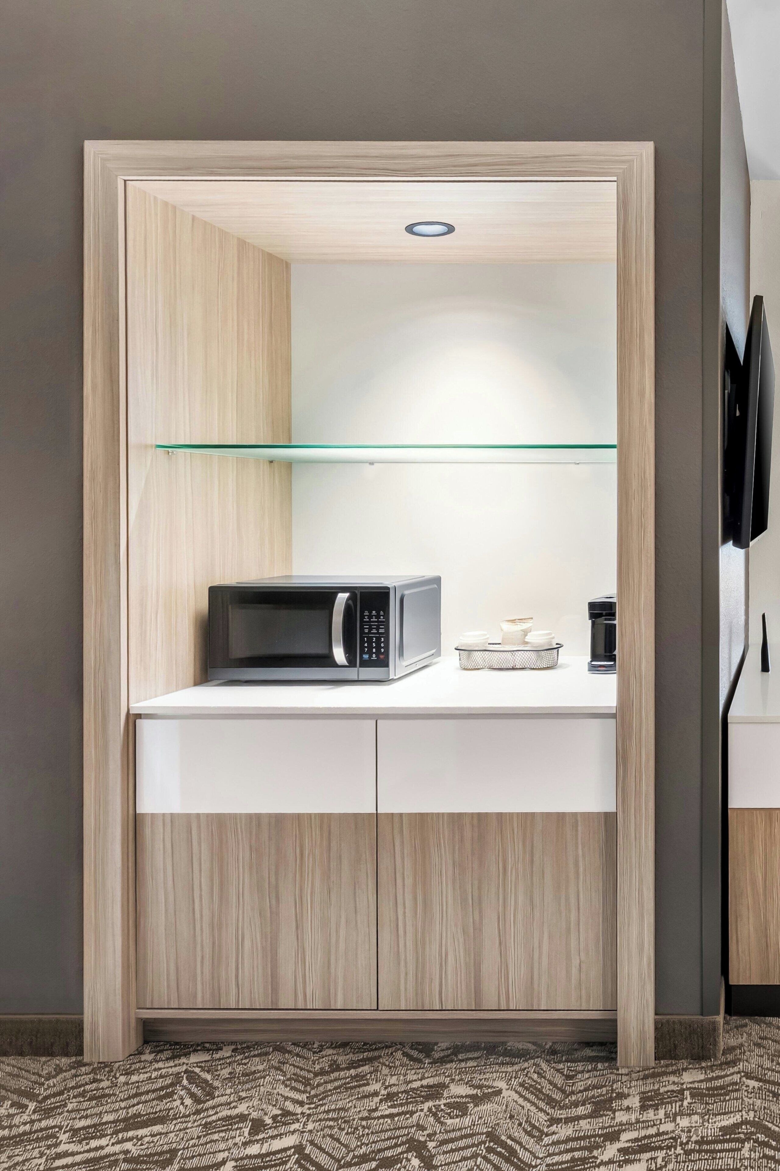 A compact kitchenette with a microwave, coffee maker, and a glass shelf.