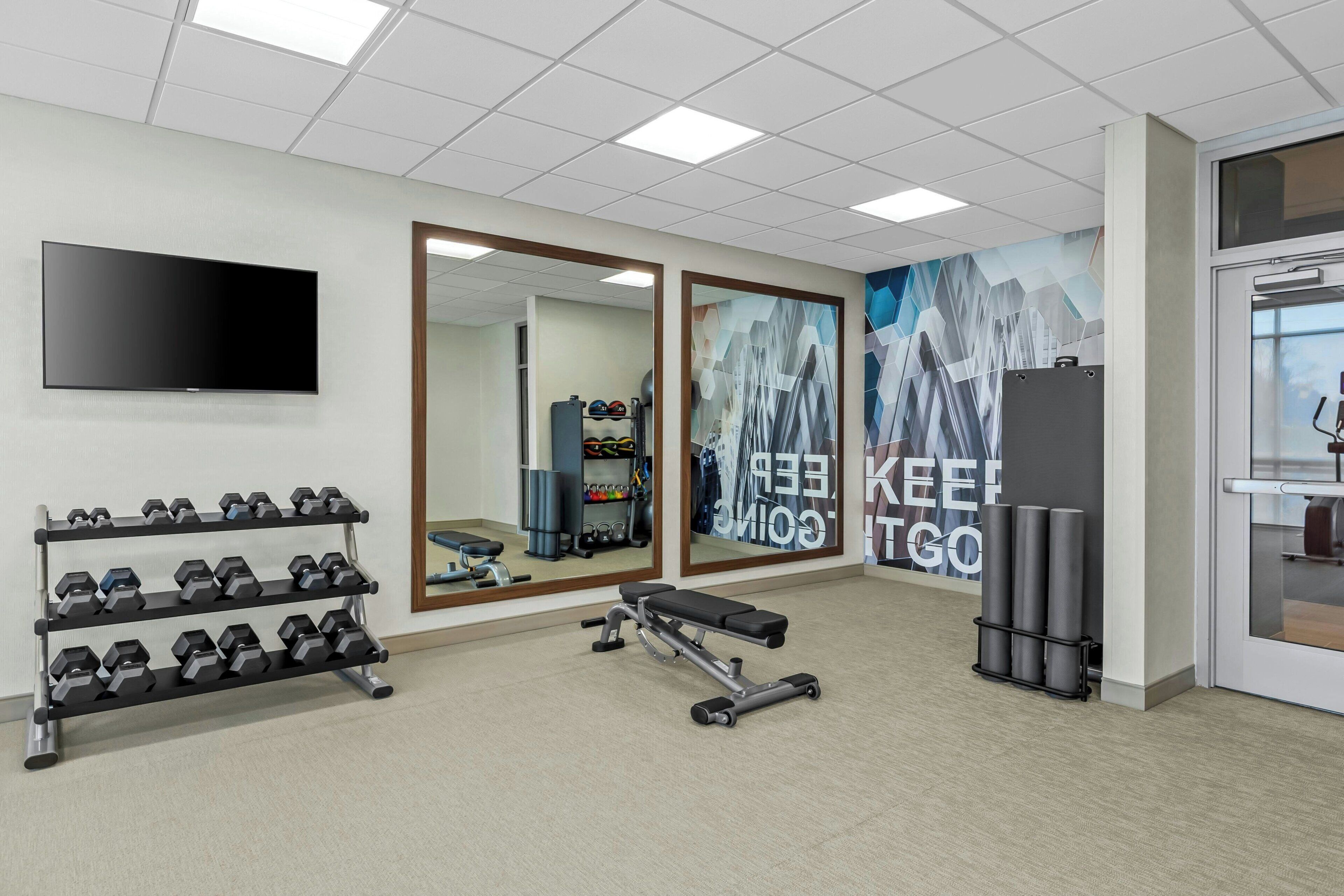 Ein Fitnessraum mit einer Bank, Hanteln, einem Fernseher und motivierenden Wandbildern.