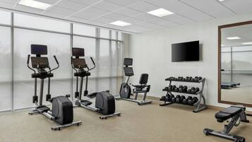Une salle de sport équipée d’appareils de cardio, d’haltères et d’un téléviseur fixé au mur.