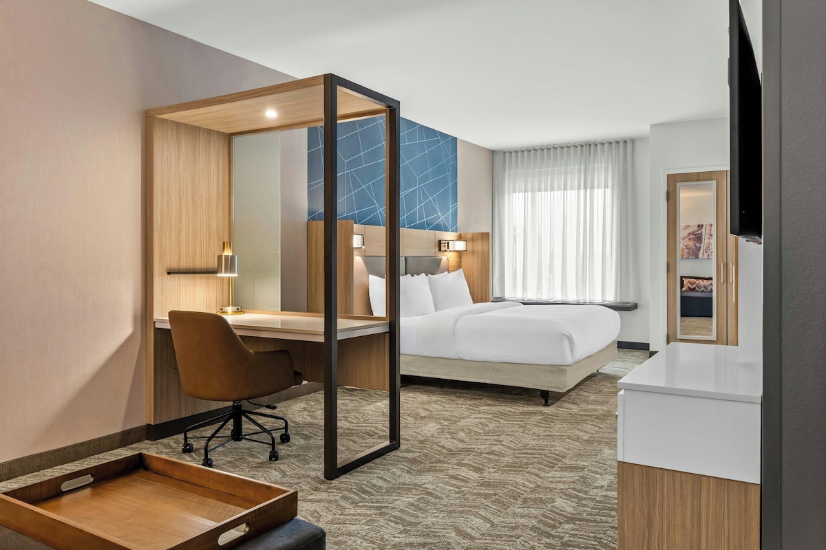 A hotel room with a bed, desk, chair, and a TV.