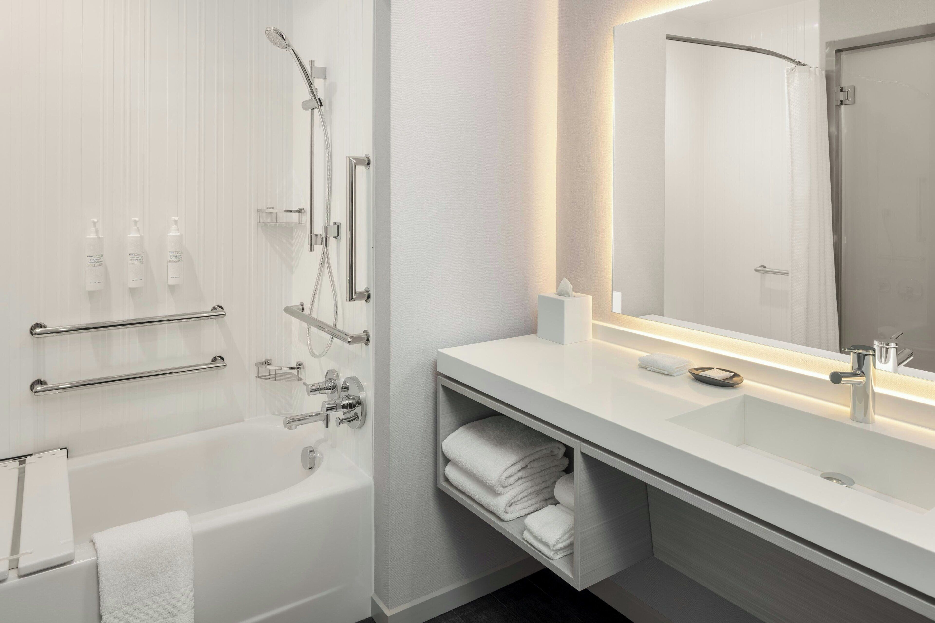 Une salle de bain moderne avec une baignoire, un grand miroir, un meuble-lavabo et un espace pour ranger les serviettes.