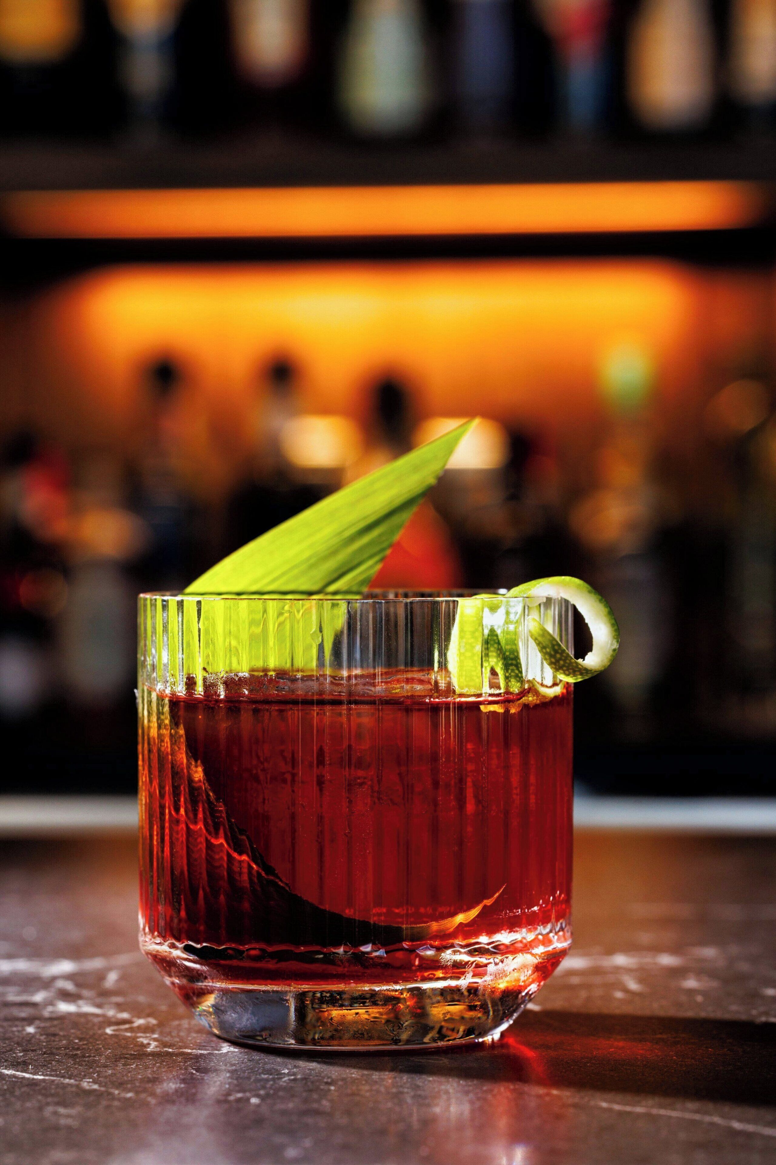 A glass of red beverage with a lime wedge garnish on a bar counter.