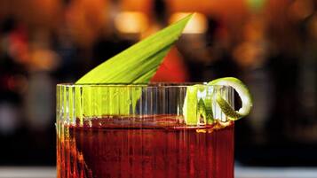 A glass of red beverage with a lime wedge garnish on a bar counter.