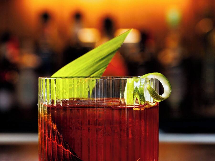 A glass of red beverage with a lime wedge garnish on a bar counter.