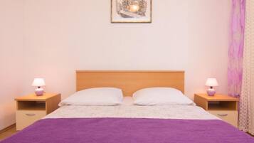 A bedroom with a wooden headboard, two bedside tables with lamps, a purple bedspread, and a framed picture on the wall.