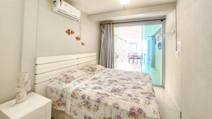 A bedroom with a bed, a nightstand, an air conditioning unit, a window with curtains, and a view of an outdoor area. - Condomínio Esmeralda do Mar (Ipojuca)