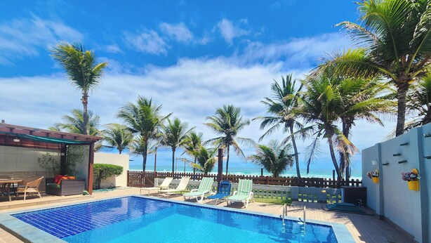 A swimming pool with lounge chairs and palm trees, overlooking a beach. - Condomínio Esmeralda do Mar (Ipojuca)