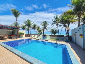A swimming pool with lounge chairs and palm trees, overlooking a beach. - Condomínio Esmeralda do Mar (Ipojuca)