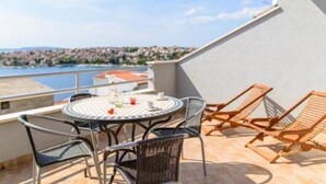 A balcony with a round table and chairs, overlooking a coastal cityscape. - Apartments Nela (Okrug)