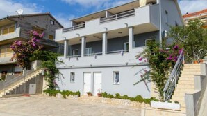A modern two-story building with balconies, a staircase, and potted plants. - Apartments Nela (Okrug)