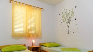 A room with two wooden beds, a nightstand with a lamp, and a window with yellow curtains. - Apartments Nela (Okrug)