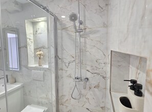 A modern bathroom with a glass-enclosed shower, marble walls, a vanity with a mirror, and a small window. - Penthouse Apartment Dijana (Dubrovnik)