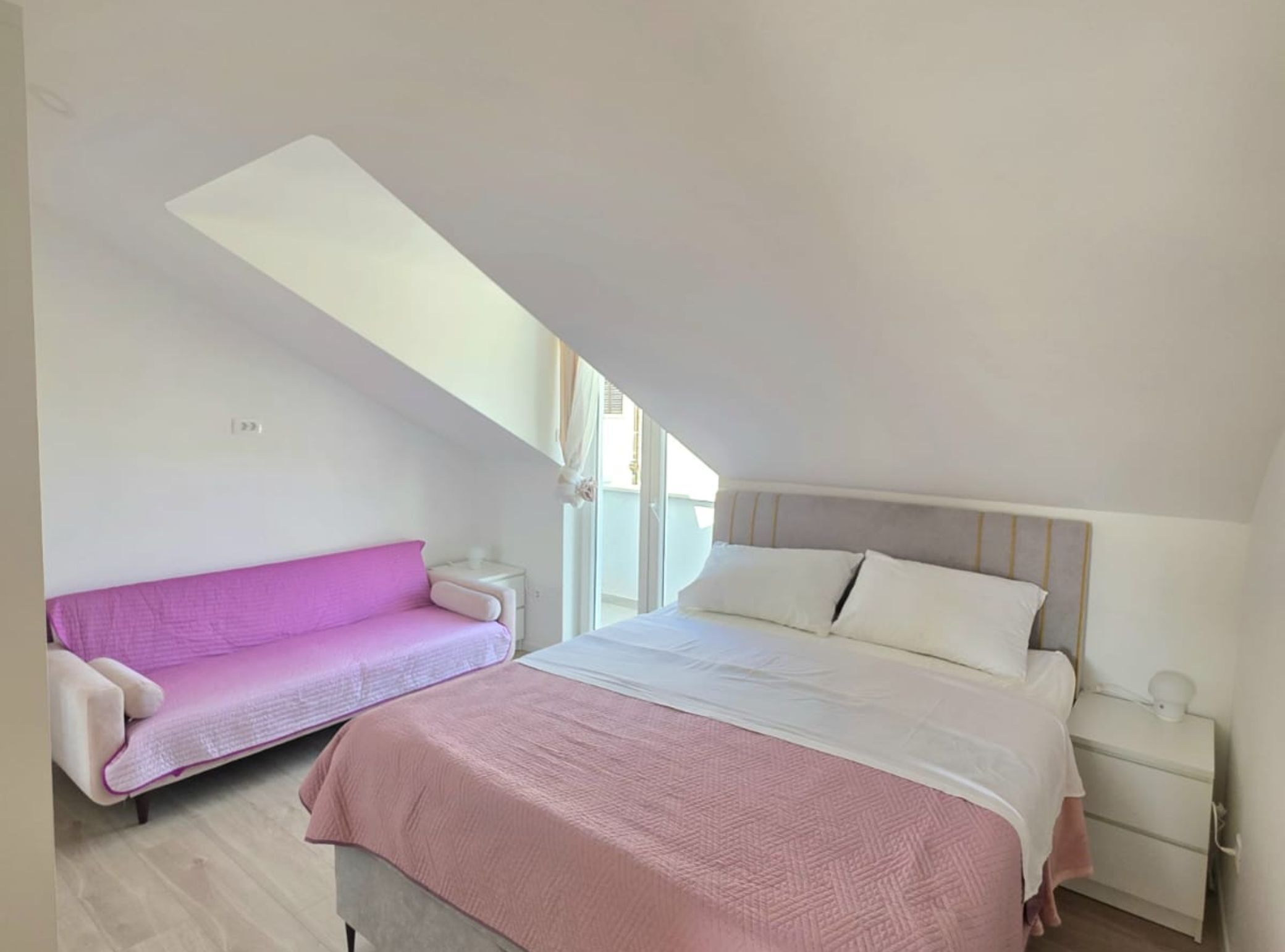 Un dormitorio con cama, sofá rosa y mesita de noche.