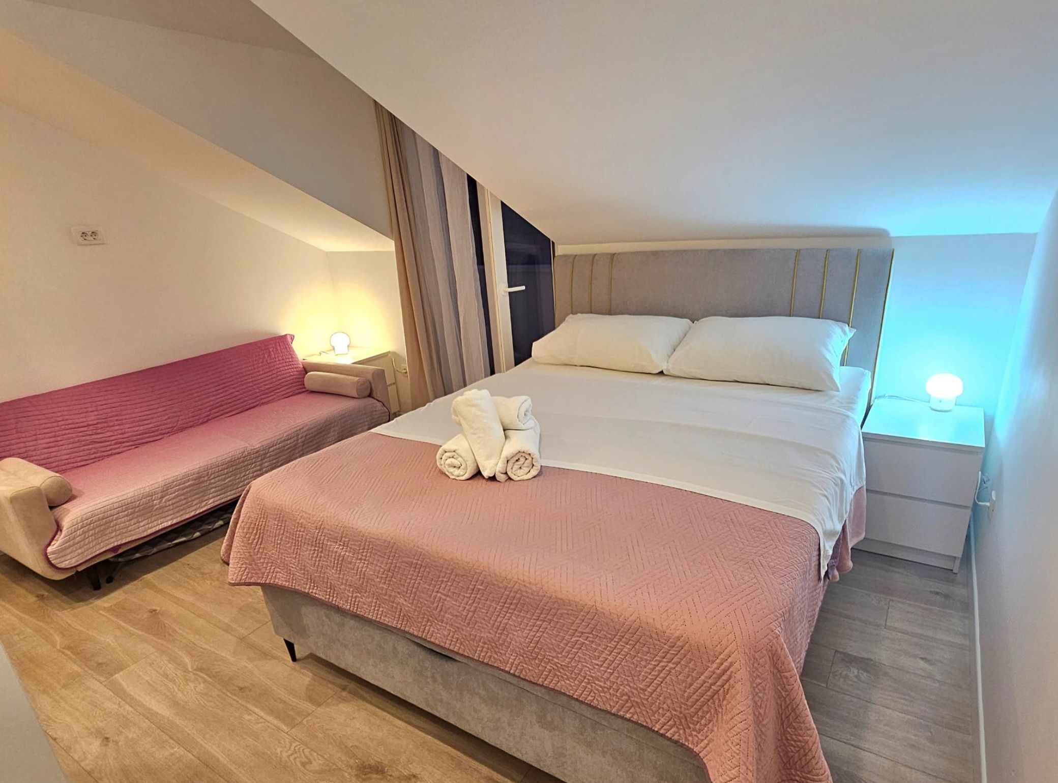 A hotel room with a bed, a sofa, and a nightstand with a lamp.
