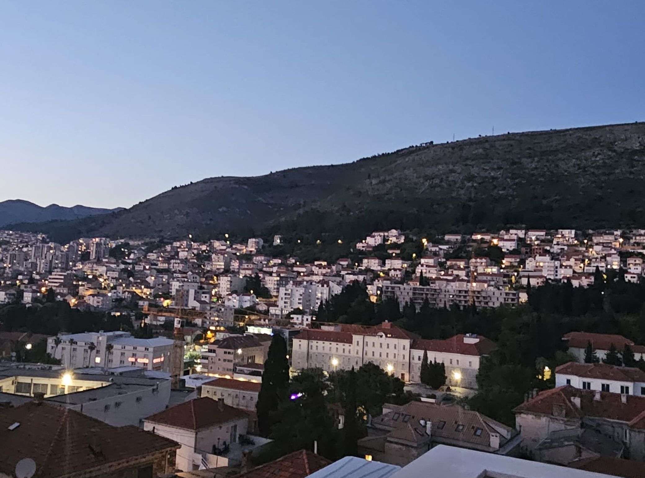 Un paisaje urbano al atardecer con edificios y una colina en el fondo.