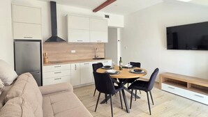 Una cocina moderna con armarios blancos, horno empotrado y comedor con mesa redonda y sillas.