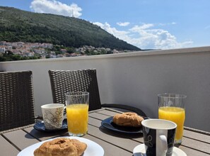 A table with breakfast items including croissants, orange juice, and coffee, set against a scenic view of a hillside town. - Penthouse Apartment Dijana (Dubrovnik)