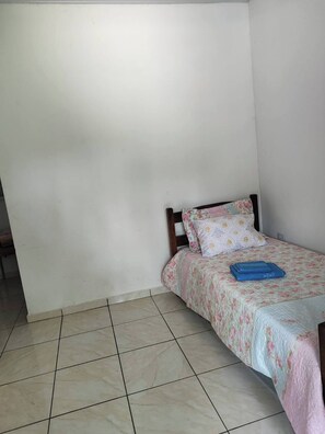 Ein kleines, ordentlich eingerichtetes Schlafzimmer mit einem Einzelbett, einem Holzkopfende und einer blumigen Bettdecke.