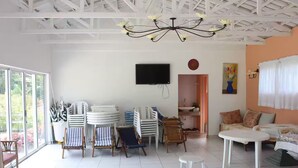 Una habitación amplia con un gran ventanal, un televisor de pantalla plana, un ventilador de techo y un sofá.