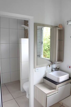 Ein modernes Badezimmer mit Toilette, Waschbecken mit Spiegel und Duschbereich.