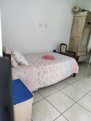Ein kleines, ordentlich eingerichtetes Schlafzimmer mit Bett, Holzschrank und Fliesenboden.