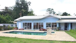 Una casa azul claro con piscina, un porche cubierto y un jardín con flores.
