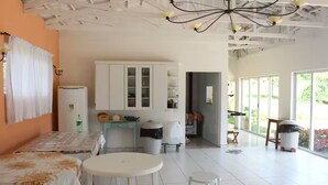 Una habitación amplia con una cama, una mesa de comedor y un taburete pequeño. Cuenta con una kitchenette con armarios y un lavabo. La habitación tiene ventanas grandes que ofrecen luz natural.