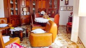 A living room with a leather sofa, a glass coffee table, wooden cabinets, and a dining area with a table and chairs. - Casa Anni `70 - Sardegna (Burgos)