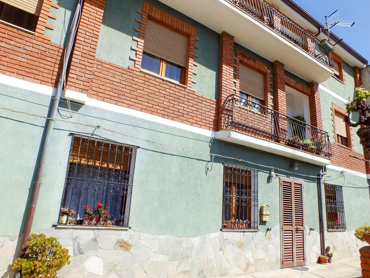 A two-story building with a stone facade, multiple windows with metal bars, and a balcony with a railing.