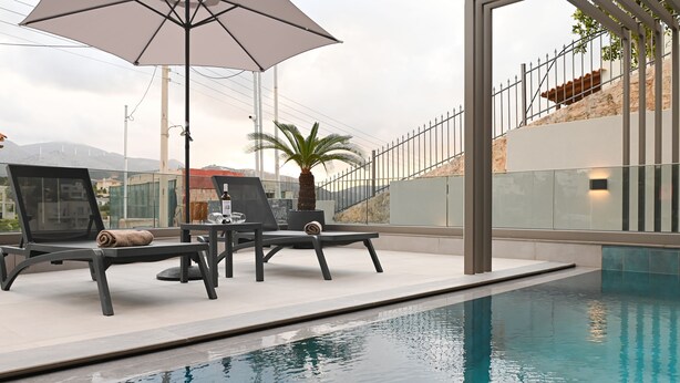 Zona junto a la piscina con sillones de descanso y una sombrilla, una palmera y vistas a un paisaje montañoso.