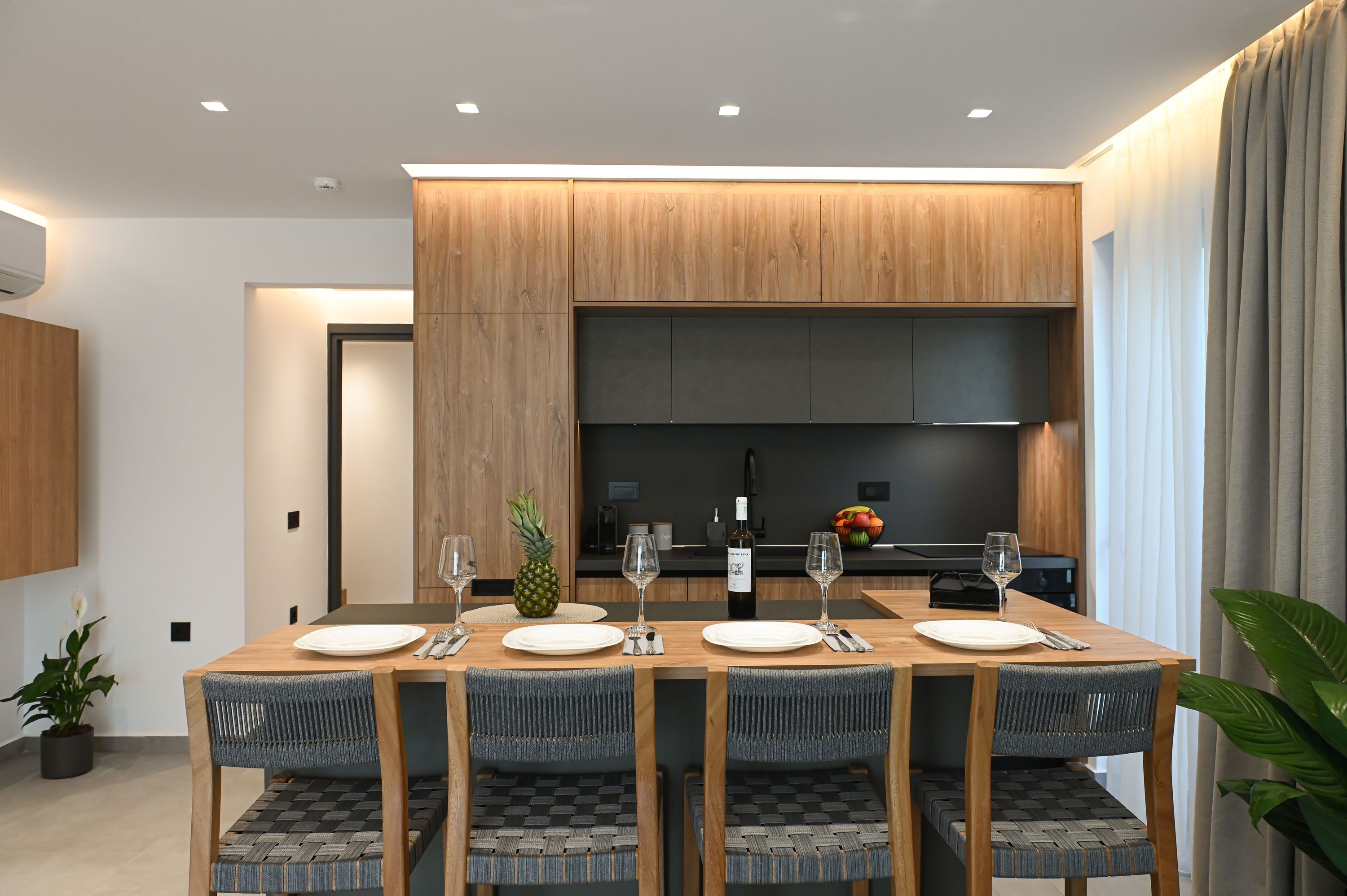 A modern dining area with a wooden table set for four, surrounded by woven chairs.