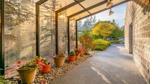 A covered walkway with potted plants and a view of trees and a car in the background.