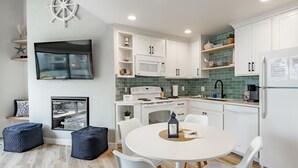 A modern kitchen with white cabinets, a microwave, and a stove. There is a dining area with a round table and chairs.