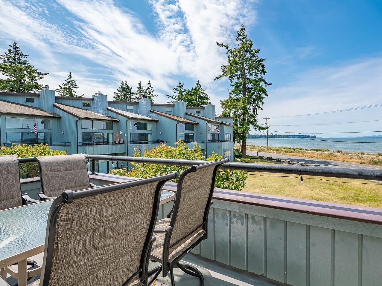 A balcony with wicker chairs and a glass table overlooking a body of water and a distant island.