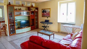 A living room with a red sofa, a television, a piano, and a window with blinds. - Villa Lucia - Apulia (Lucera)