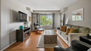 A living room with a fireplace, a sofa, a coffee table, and a TV on a stand. - The Dragonfly | Pool/Hot Tub | Lake Access | Kayak (Invermere)