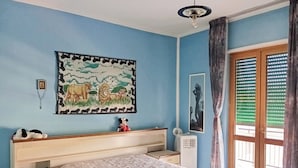 Ein Schlafzimmer mit Bett, Kommode, Nachttisch, Wand-Klimaanlage, Fenster mit Jalousien und Deckenventilator.