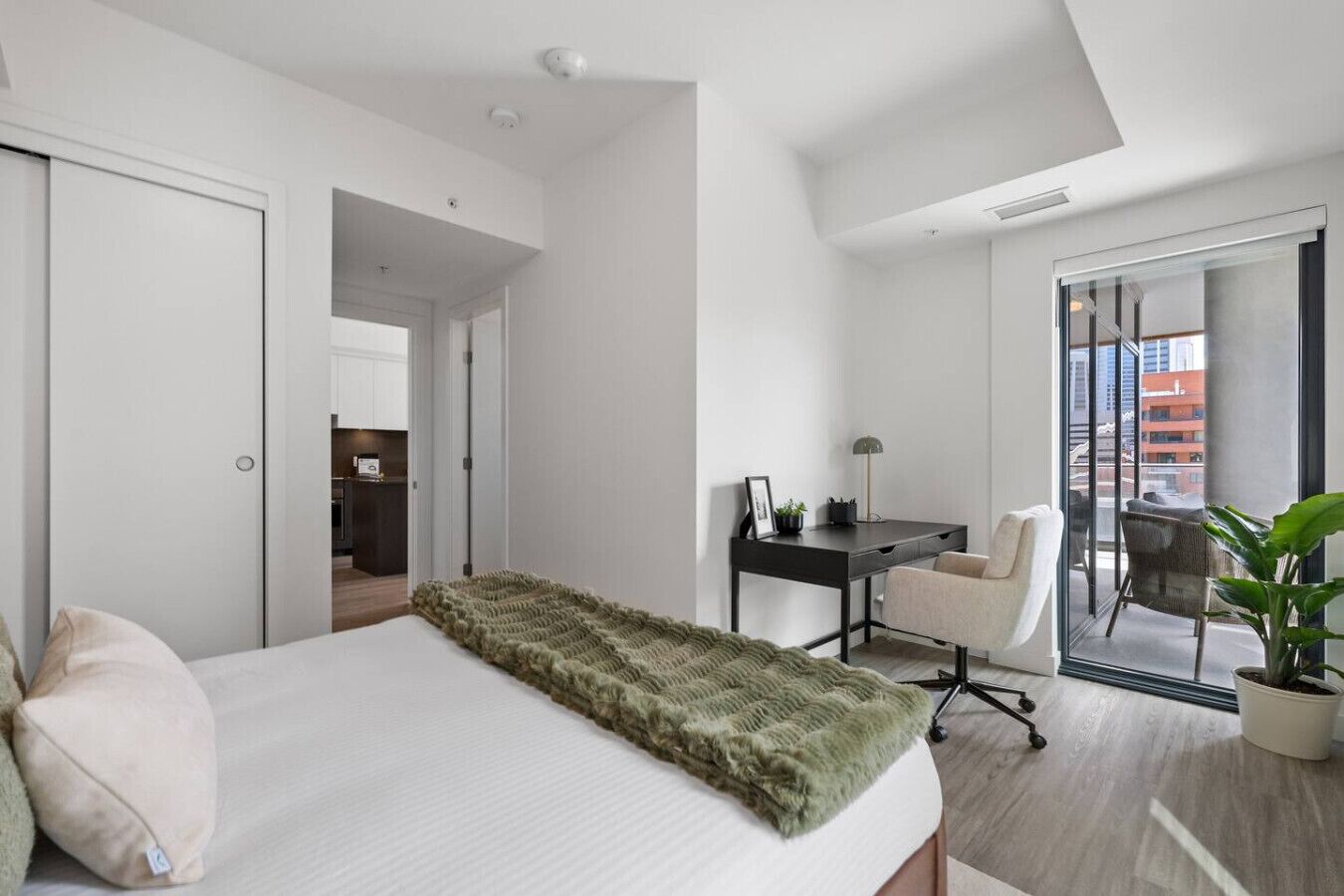 Une chambre d’hôtel moderne, dotée d’un grand lit, d’un bureau et d’une chaise. Elle dispose également d’un balcon avec vue sur la ville.