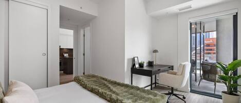 Une chambre d’hôtel moderne, dotée d’un grand lit, d’un bureau et d’une chaise. Elle dispose également d’un balcon avec vue sur la ville.