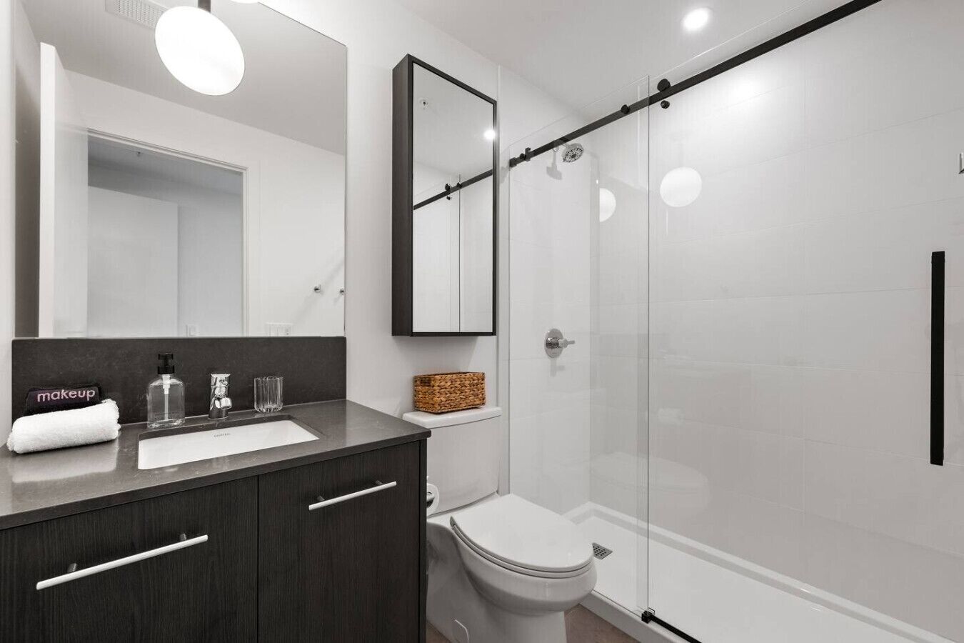 Ein modernes Badezimmer mit einem dunklen Holzwaschtisch, einer Glasdusche und einer weißen Toilette.
