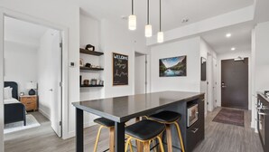 A modern kitchen with a central island, bar stools, pendant lighting, and a cityscape painting.