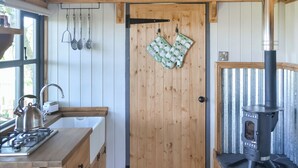 A compact kitchen with wooden cabinets, a kettle, a stove, and a wood-burning stove. - 1 bedroom accommodation in Castle Douglas (Castle Douglas)