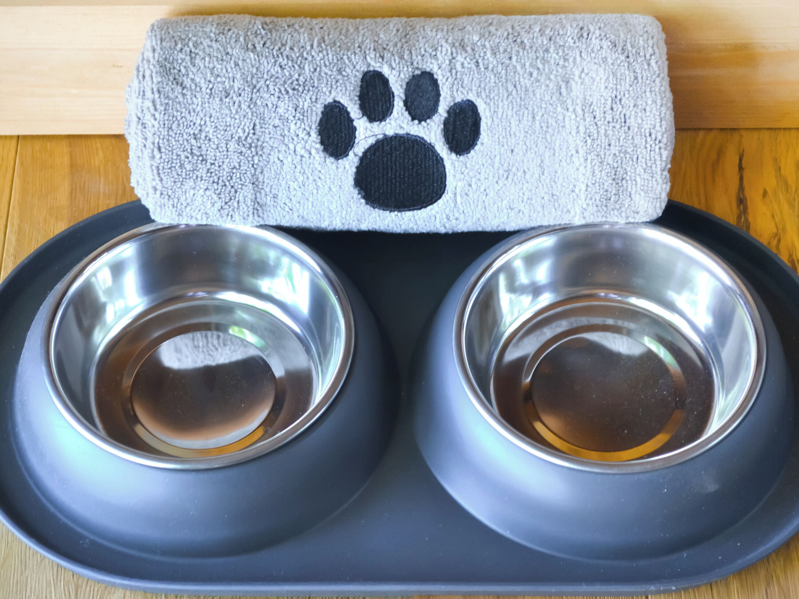 A pet feeding station with two stainless steel bowls and a grey towel with a black paw print.
