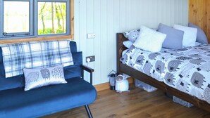 A cozy room with a bed, a blue sofa, and a window with a view of trees. - 1 bedroom accommodation in Castle Douglas (Castle Douglas)