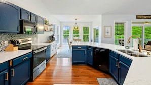 A modern kitchen with dark blue cabinets, stainless steel appliances, and large windows.