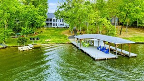 A lakeside property with a dock, a covered seating area, and a large house in the background.